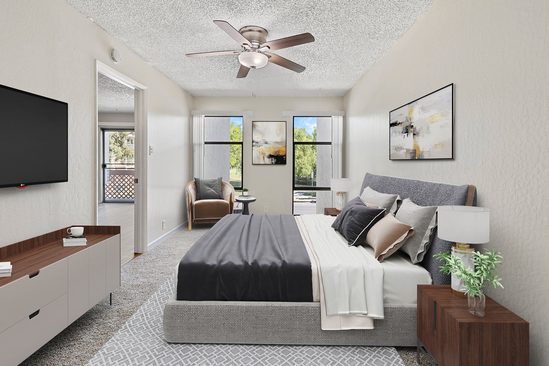 Modern living room with a gray sofa, patterned rug, glass coffee table, armchair, and wall-mounted television at Parkview Apartments.