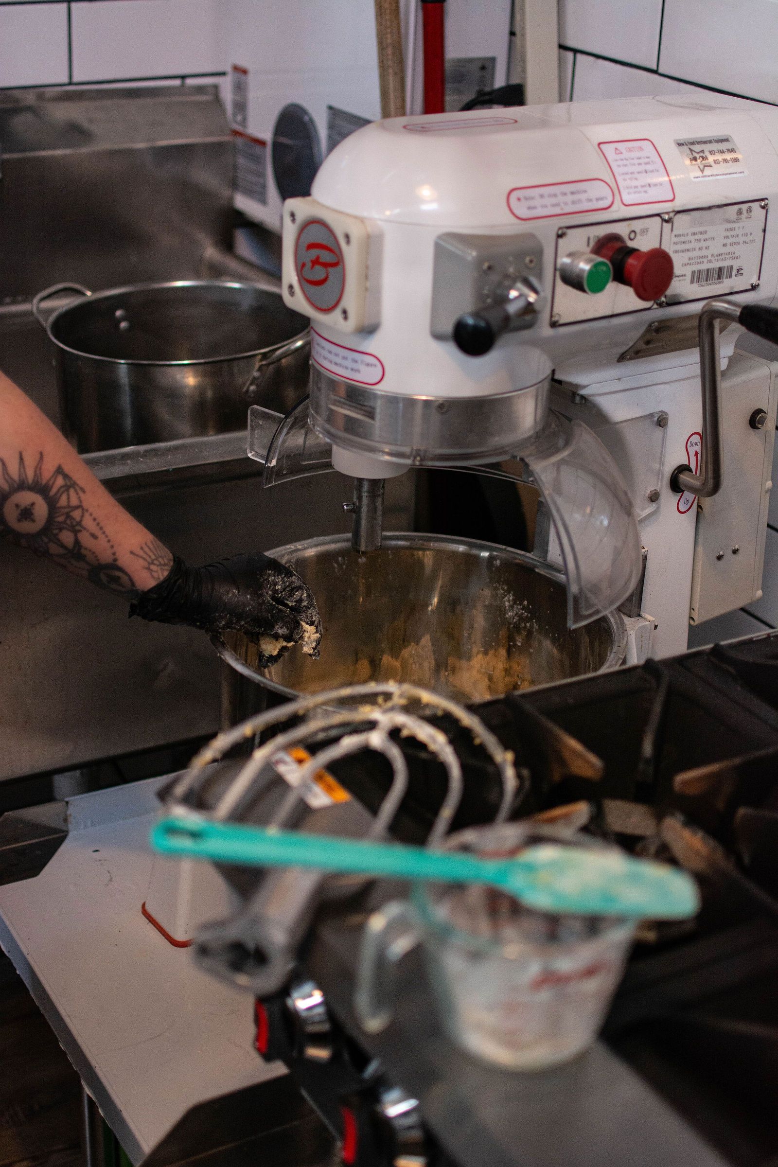 Person mixing ingredients in a large, white commercial mixer in a kitchen.