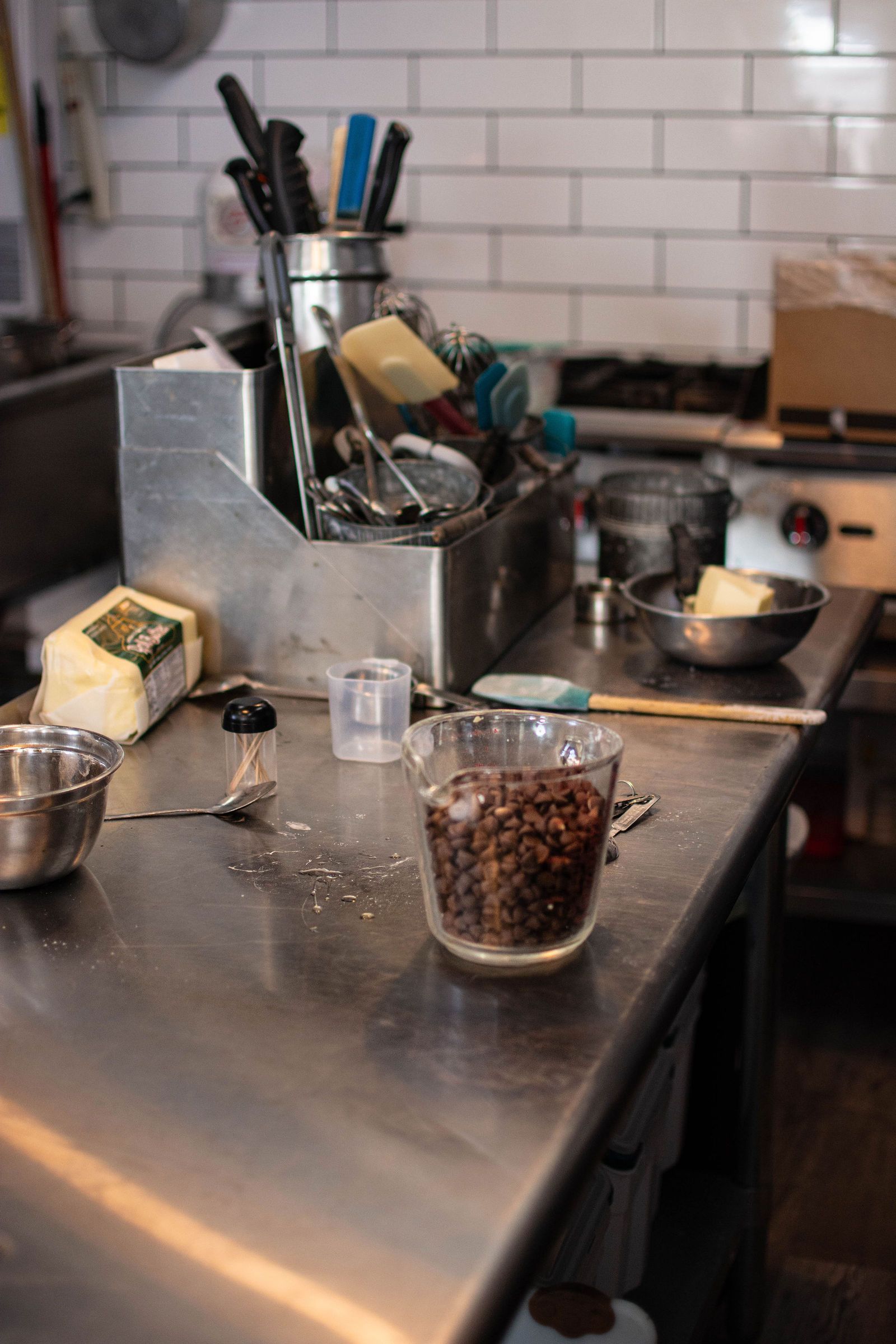 Stainless steel kitchen countertop with cooking tools, cheese, a glass of beans.
