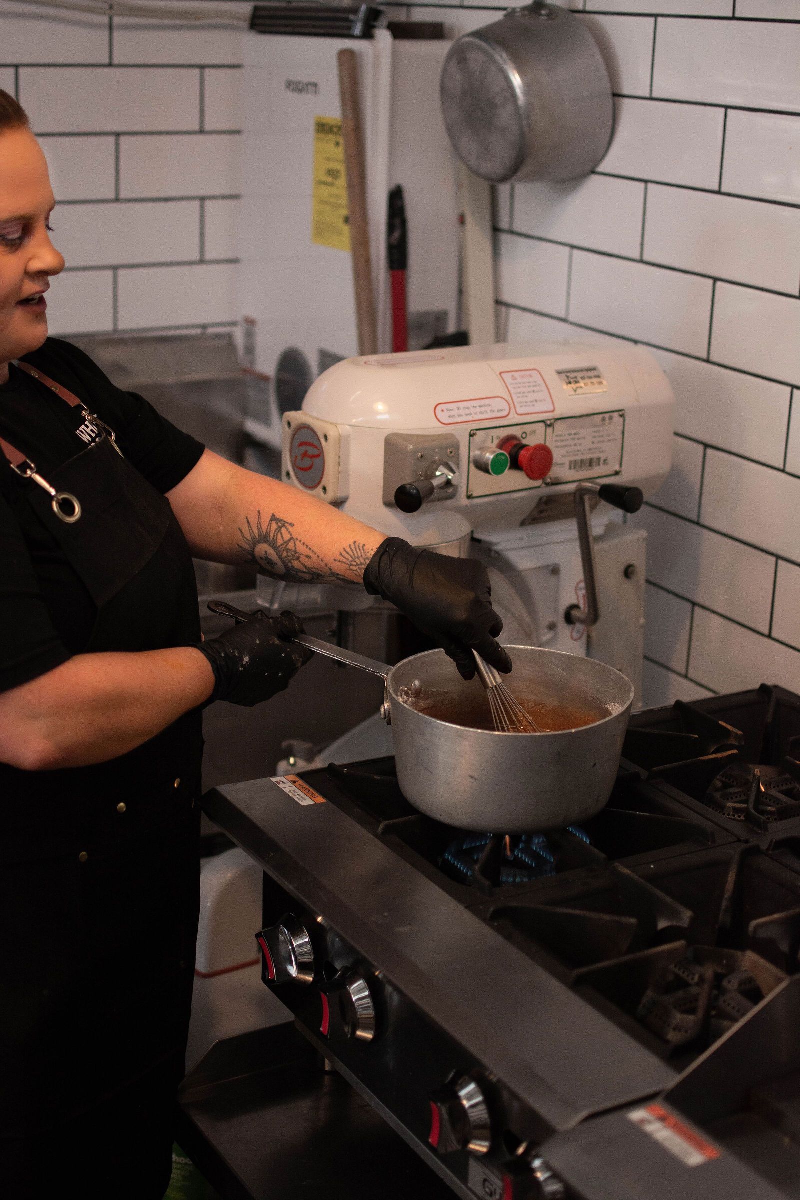 Person stirring food in a pot on a gas stove in a kitchen.