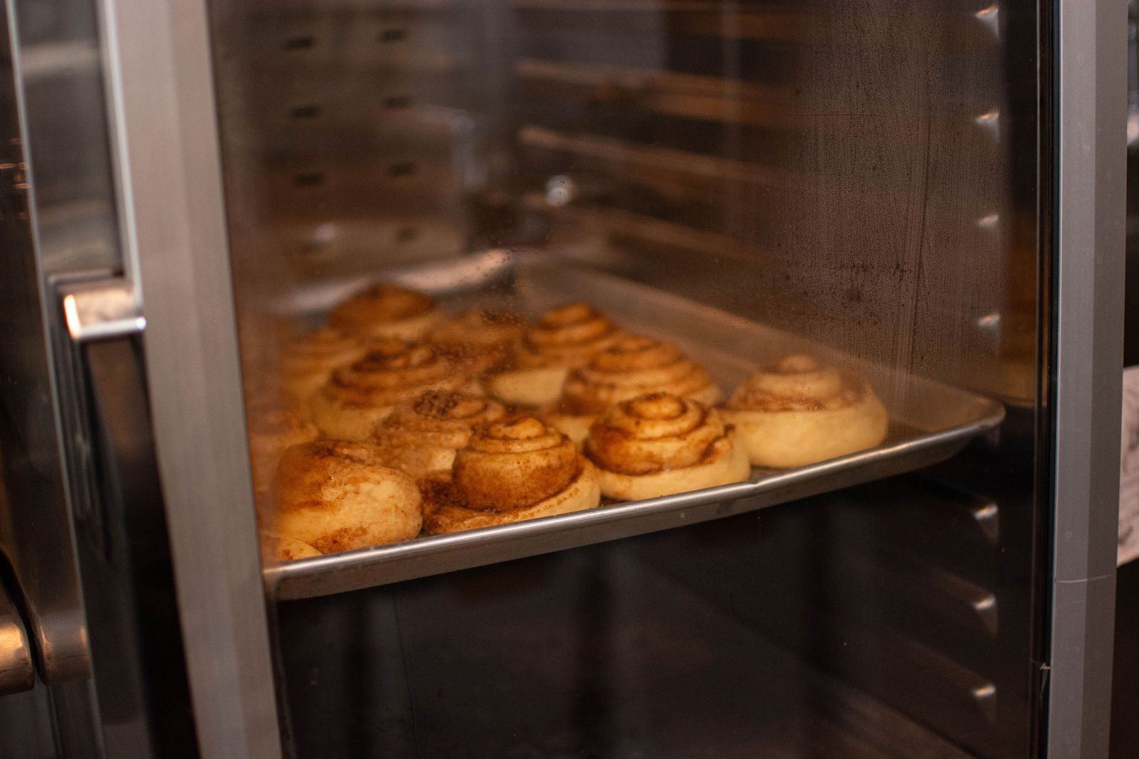 Cinnamon rolls baking in an oven on a metal tray.