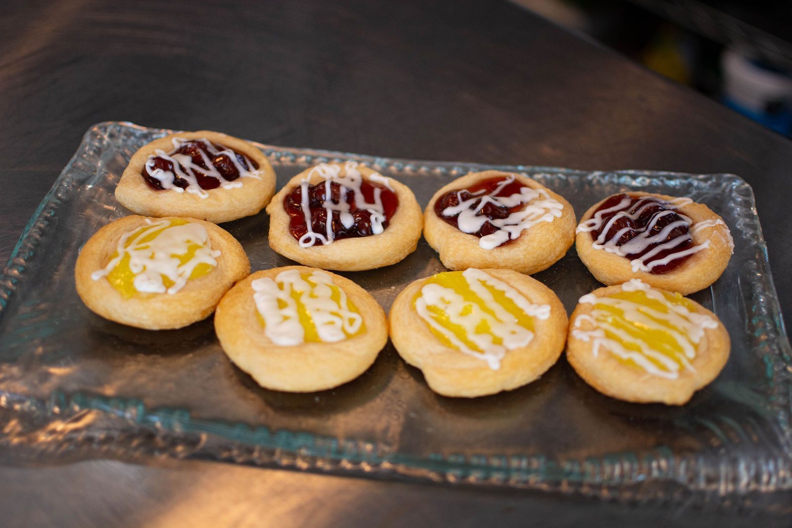 Thumbprint cookies, some with jam and white icing, others with yellow lemon icing, on a glass plate.