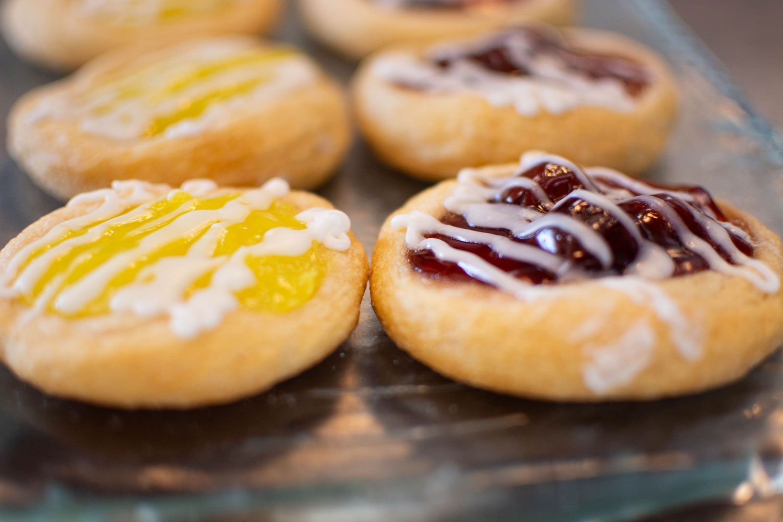 Close-up of pastries with yellow and red fruit fillings, drizzled with white icing, on a glass tray.