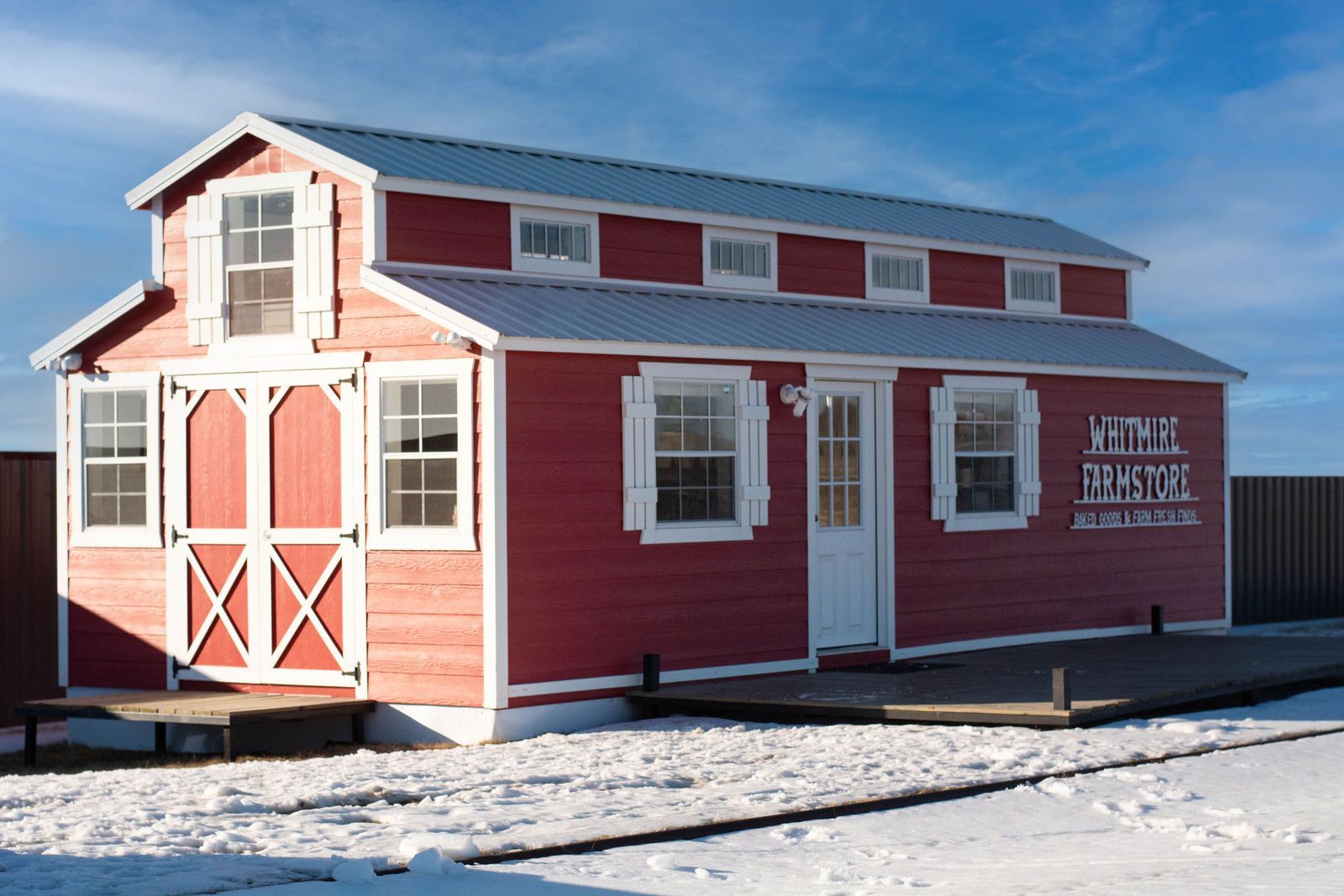 Red tiny house with white trim and snow, business sign on the side, under a blue sky.