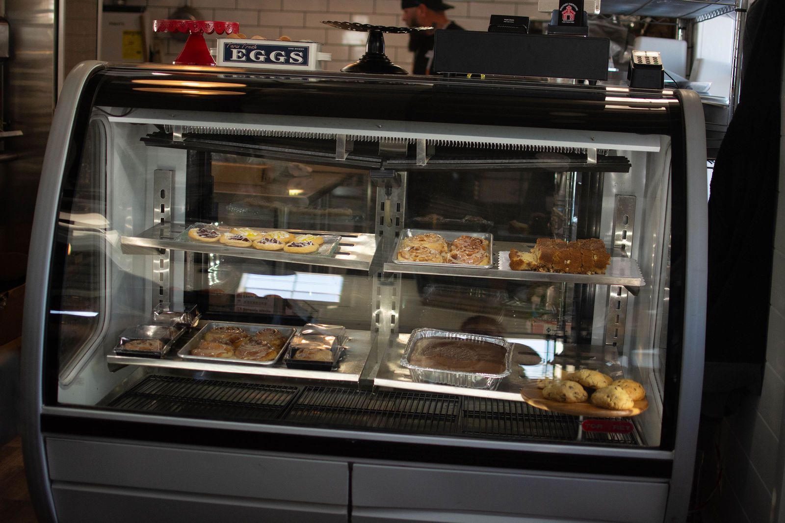 Display case filled with baked goods in a cafe. The case is stainless steel, and lit inside.