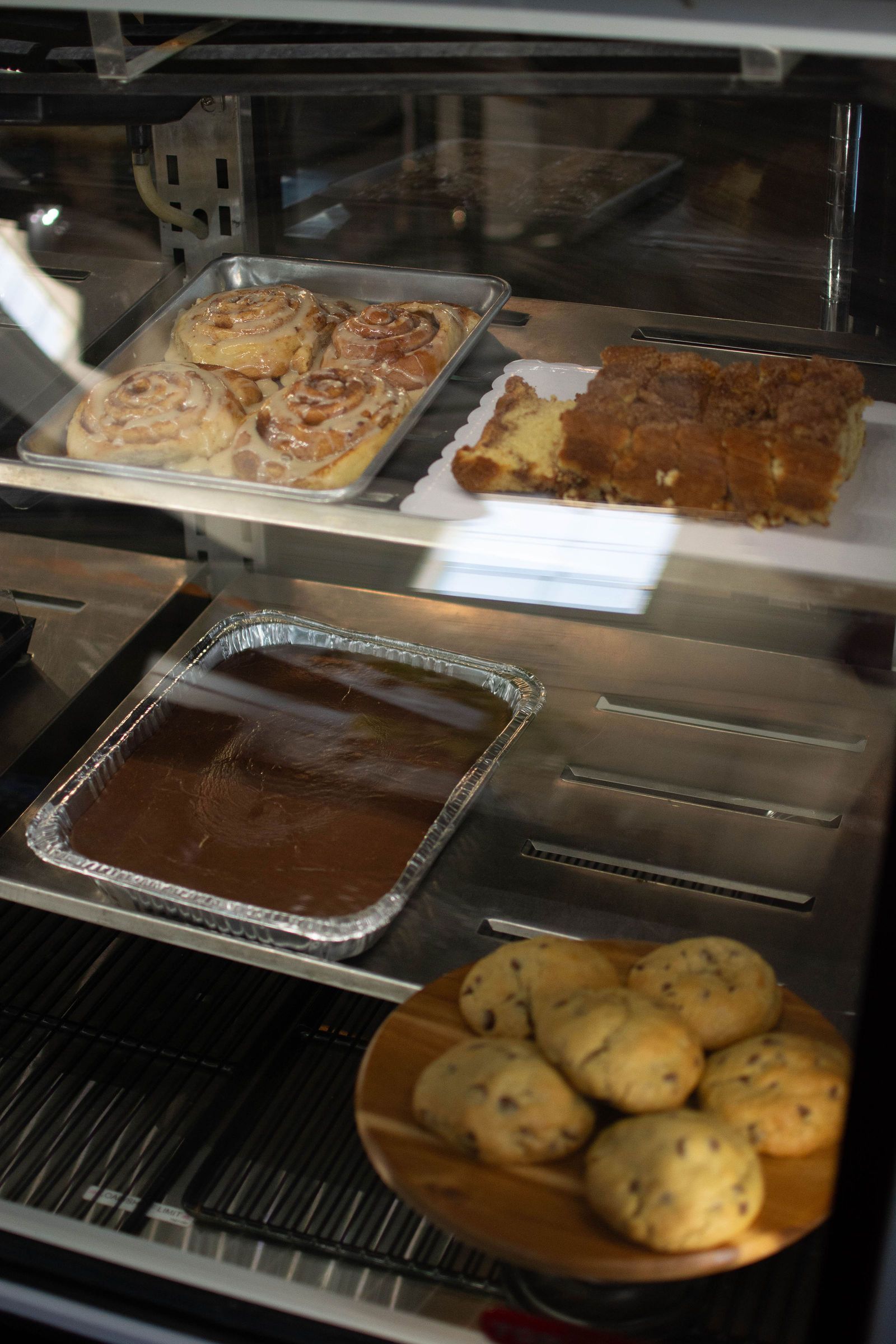 Baked goods in a display case: cinnamon rolls, coffee cake, brownies, and chocolate chip cookies.