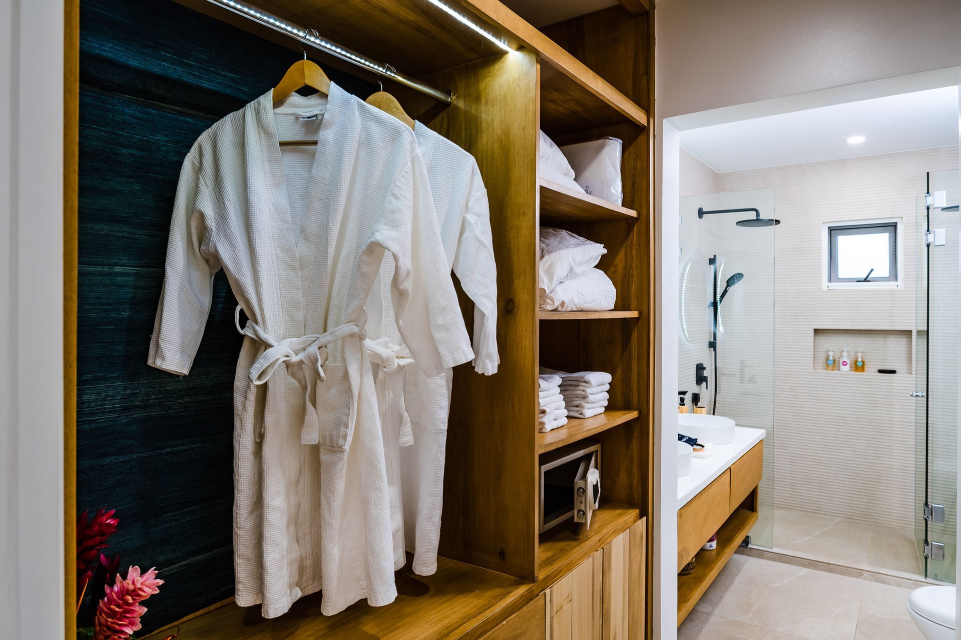 Two bathrobes are hanging in a walk in closet next to a bathroom.