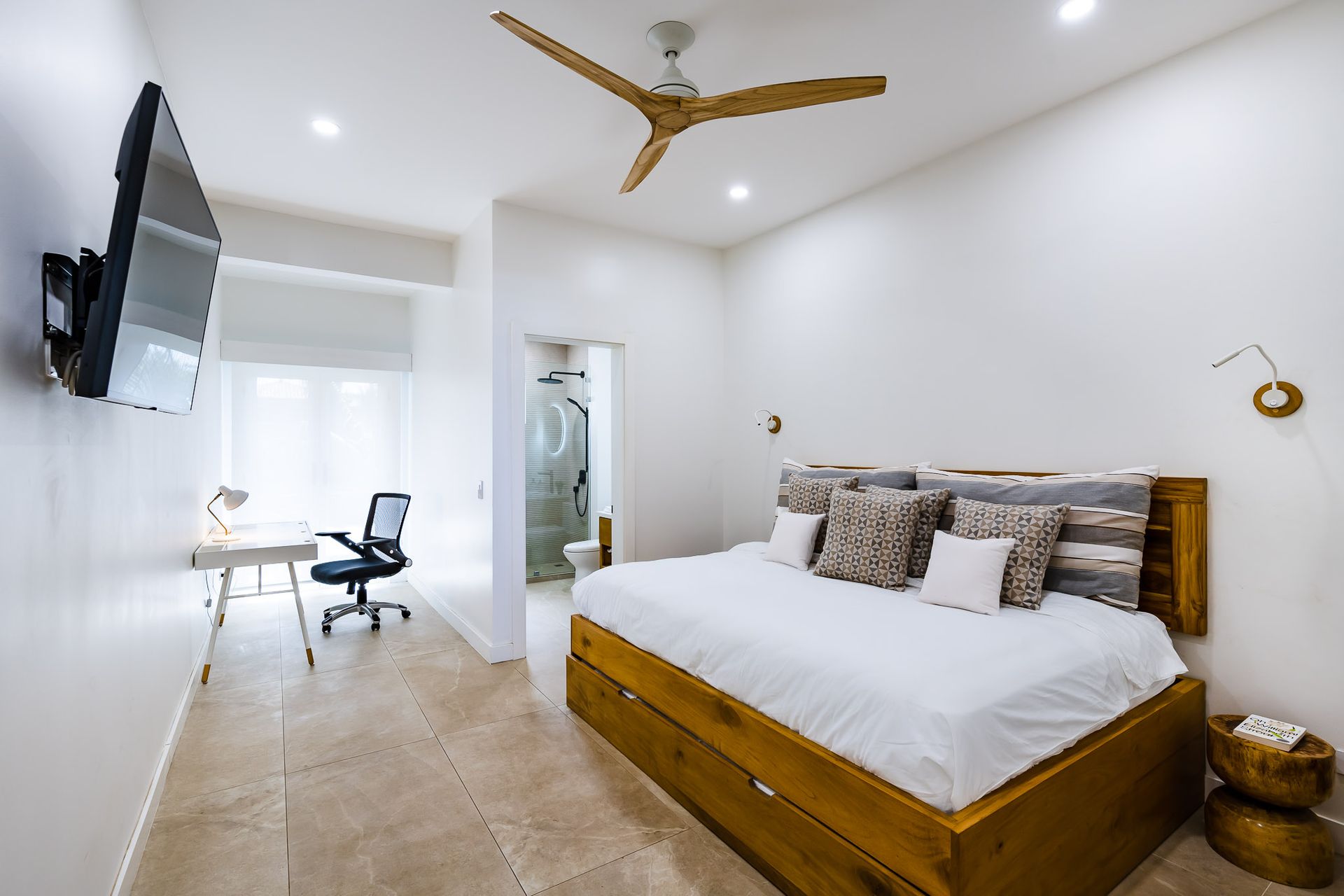 A bedroom with a king size bed , desk , television and ceiling fan.