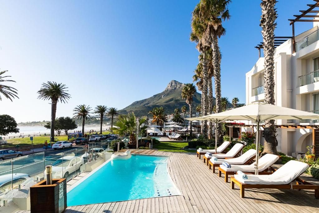 Hotel pool with lounge chairs, palm trees, and mountain views under a clear sky.