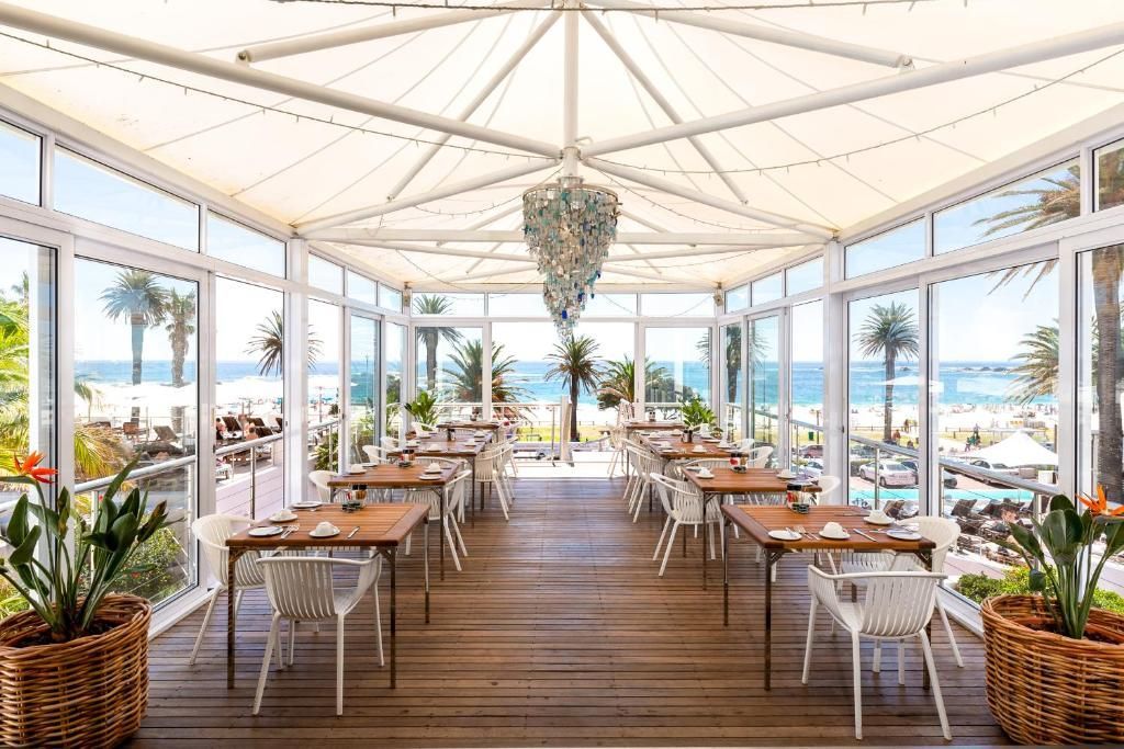 Restaurant with tables and chairs, glass walls, ocean view, white canopy, chandelier, wooden floor.