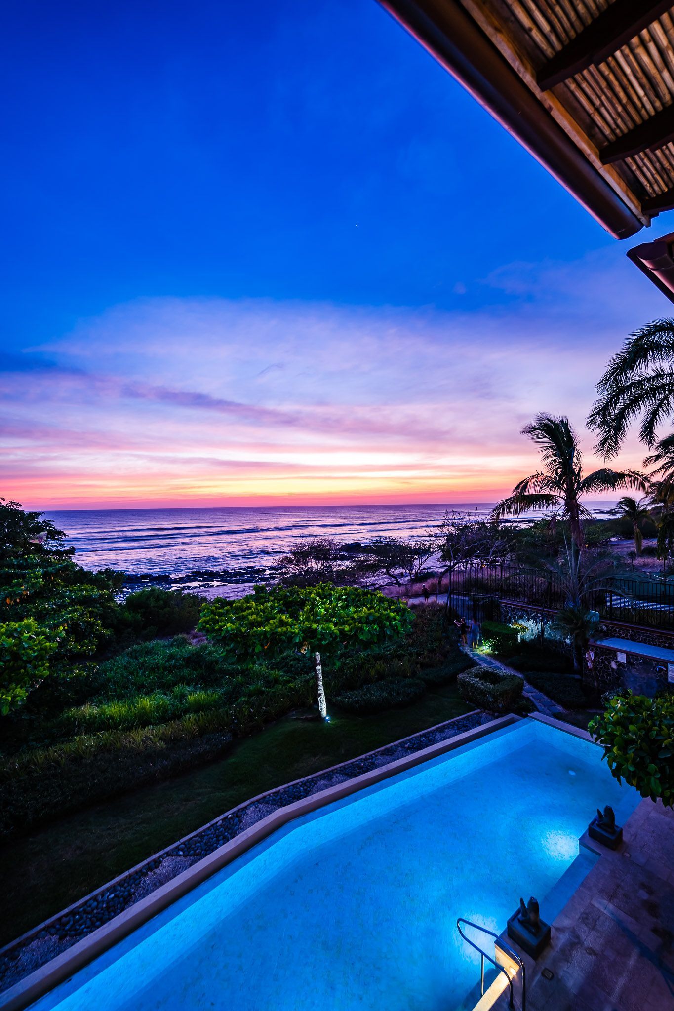 A large swimming pool with a view of the ocean at sunset.