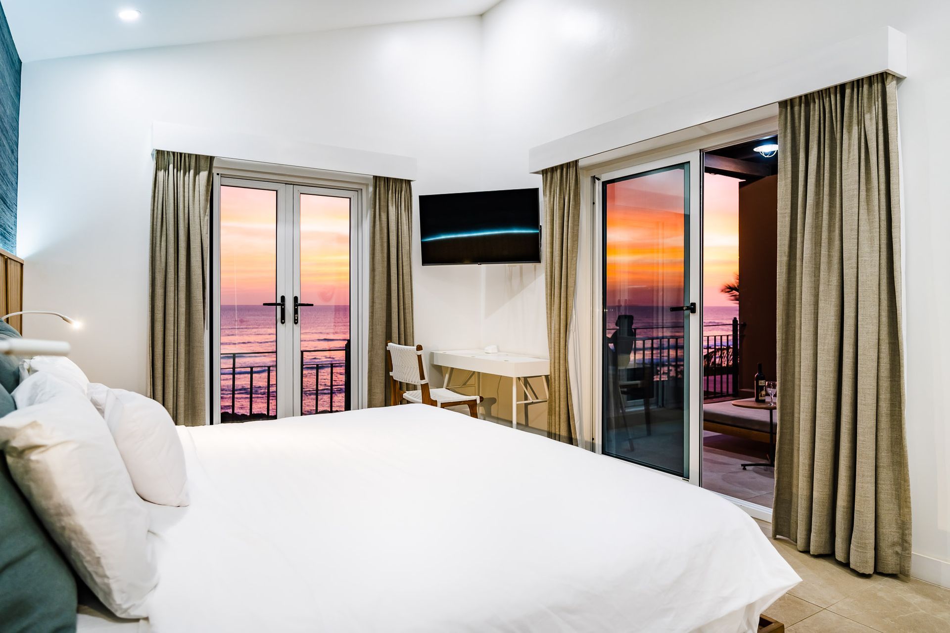 A hotel room with a king size bed and a balcony overlooking the ocean.