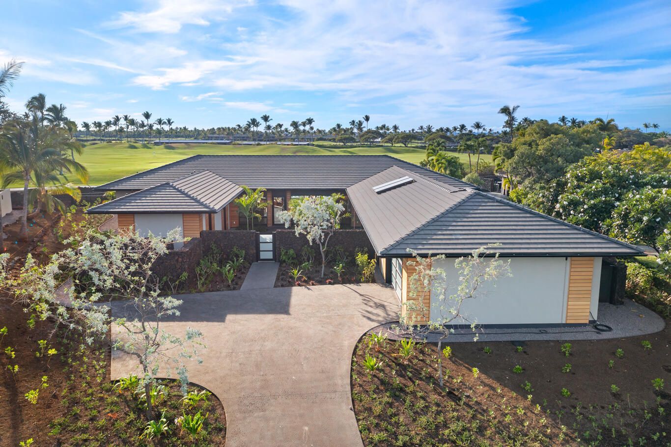 An aerial view of a house with a driveway leading to it surrounded by trees.