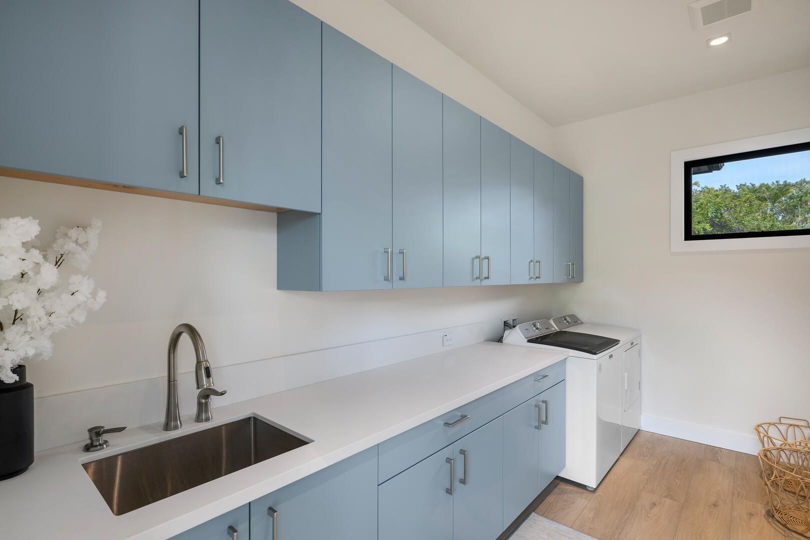 A laundry room with blue cabinets , a sink , a washer and dryer , and a window.