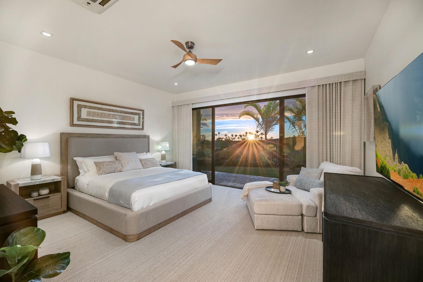 A bedroom with a large bed , sliding glass doors , a ceiling fan and a flat screen tv.