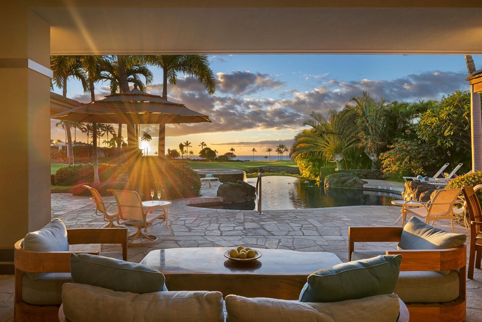 Sunset view from a patio, with seating area and a pool overlooking a golf course and ocean.