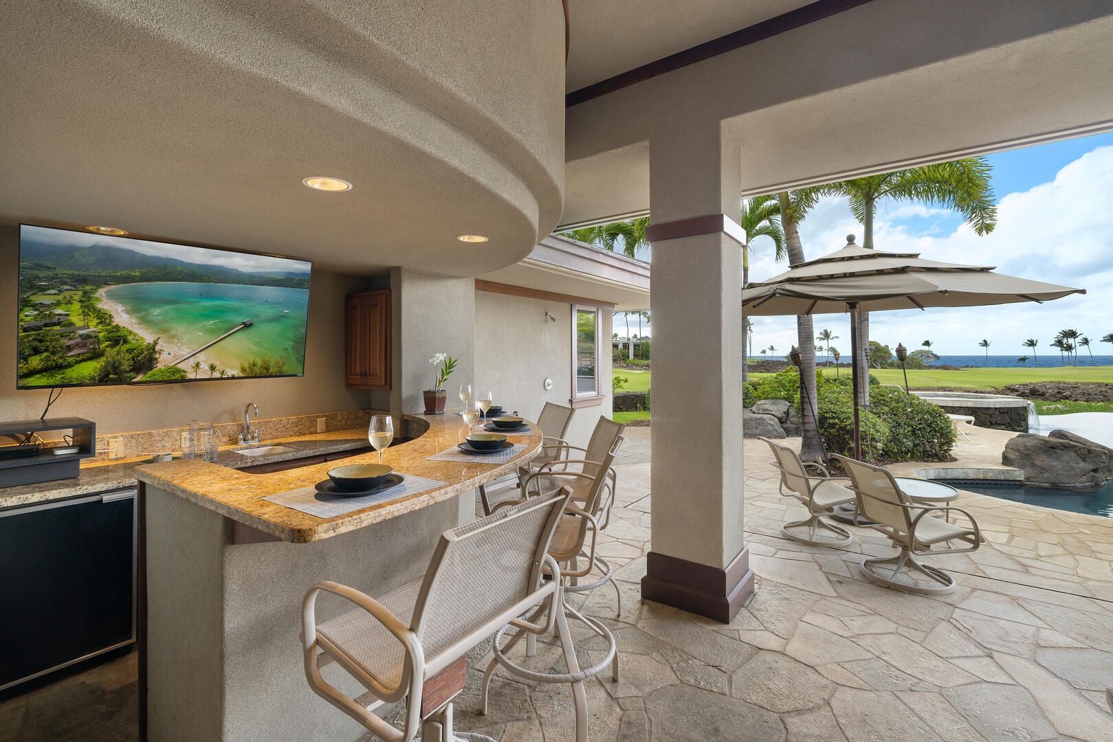 Outdoor bar with a curved countertop, stools, a TV, and a view of the ocean.