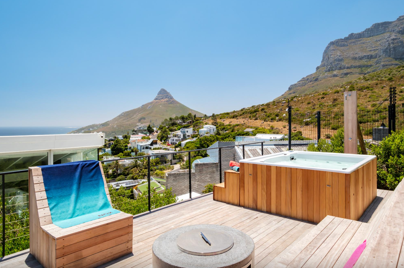 Wooden deck with hot tub overlooking a city and mountain under a clear sky.