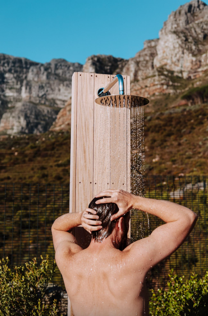Man showering outdoors with mountain backdrop.