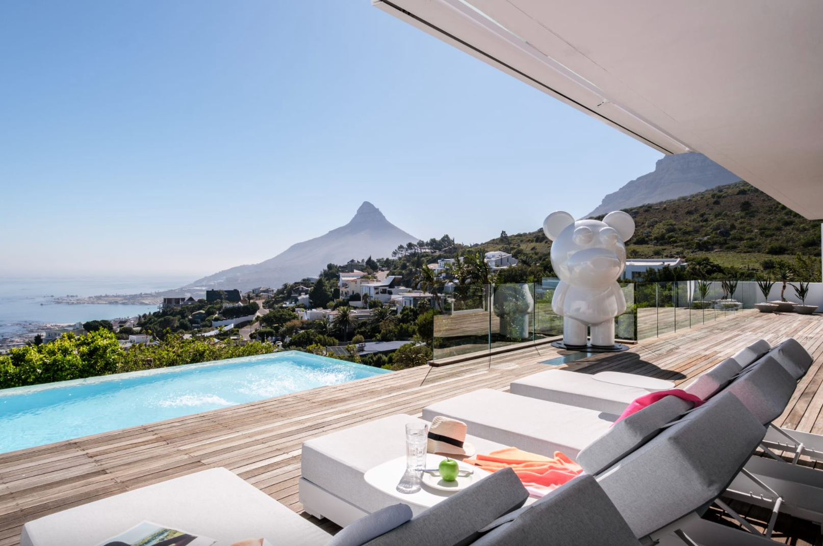 Luxury outdoor deck with pool overlooking a city and mountain under a clear blue sky.