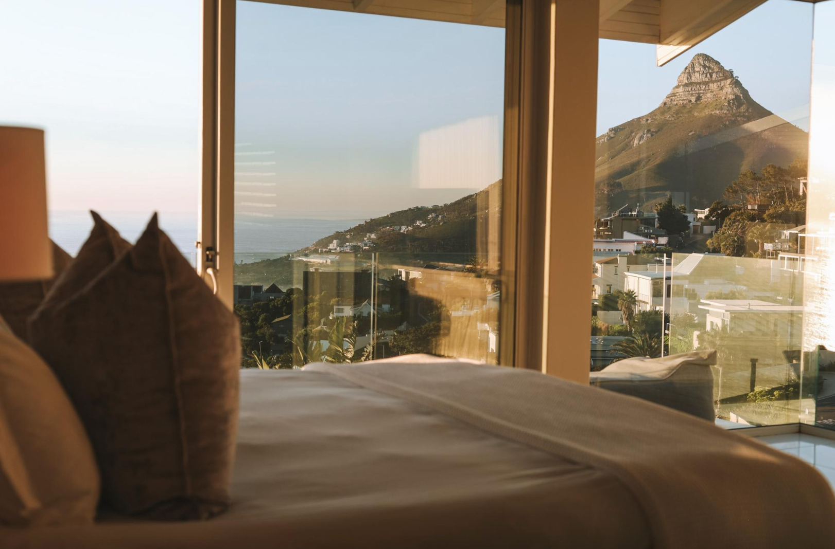 Bedroom with mountain view through large windows; bed and pillows in the foreground.