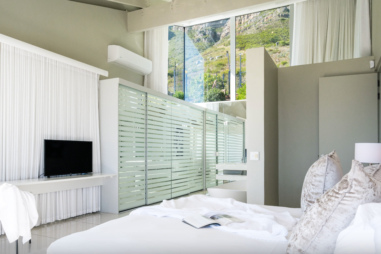 Bedroom with white bedding, TV, frosted glass closet, and mountain view.