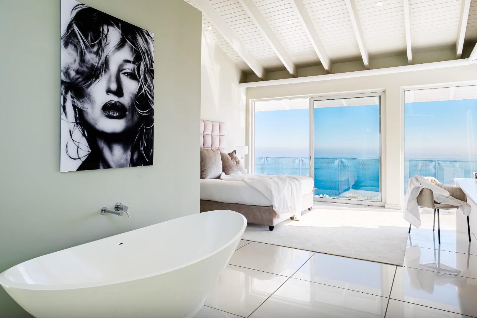 Luxury bathroom with ocean view, bathtub, bed, and artwork of a woman.