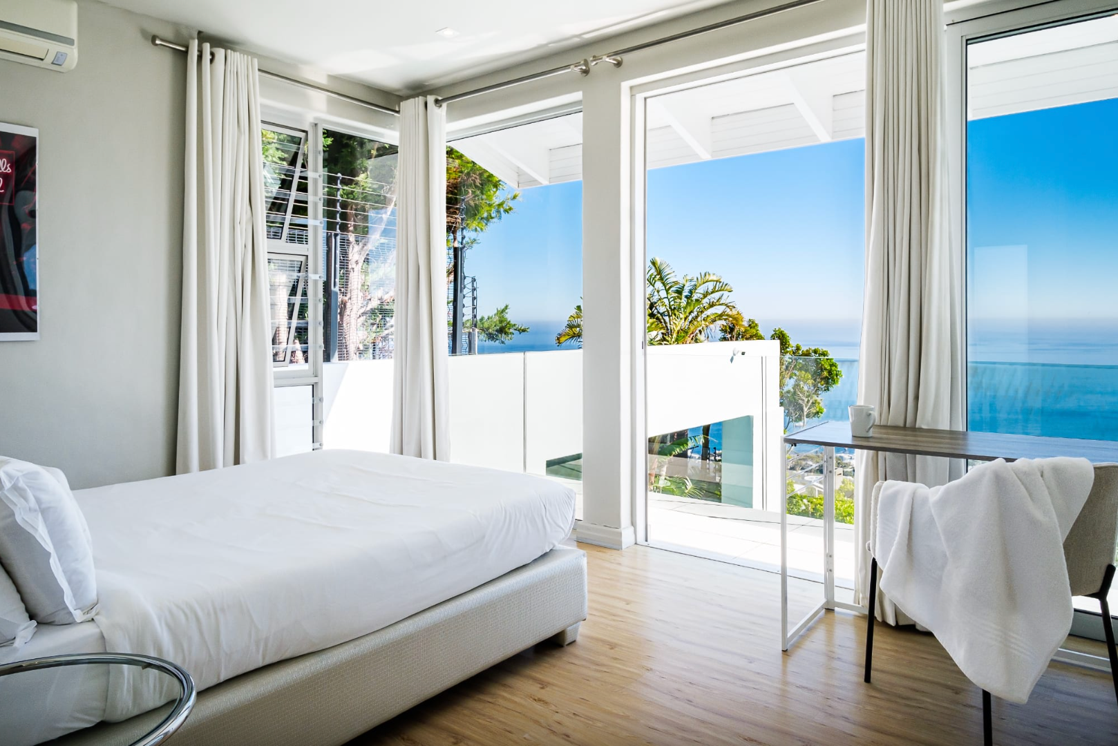 Bright bedroom with white bed, large windows overlooking ocean view.