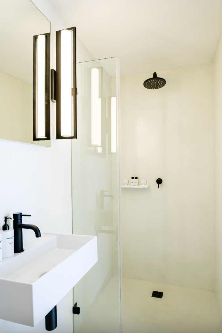 Modern white bathroom with black fixtures. Rectangular sink, glass shower, and vertical light fixture.