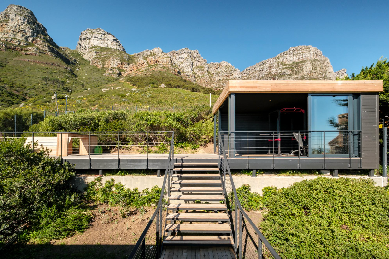 Modern cabin with deck and stairs, with mountain backdrop.