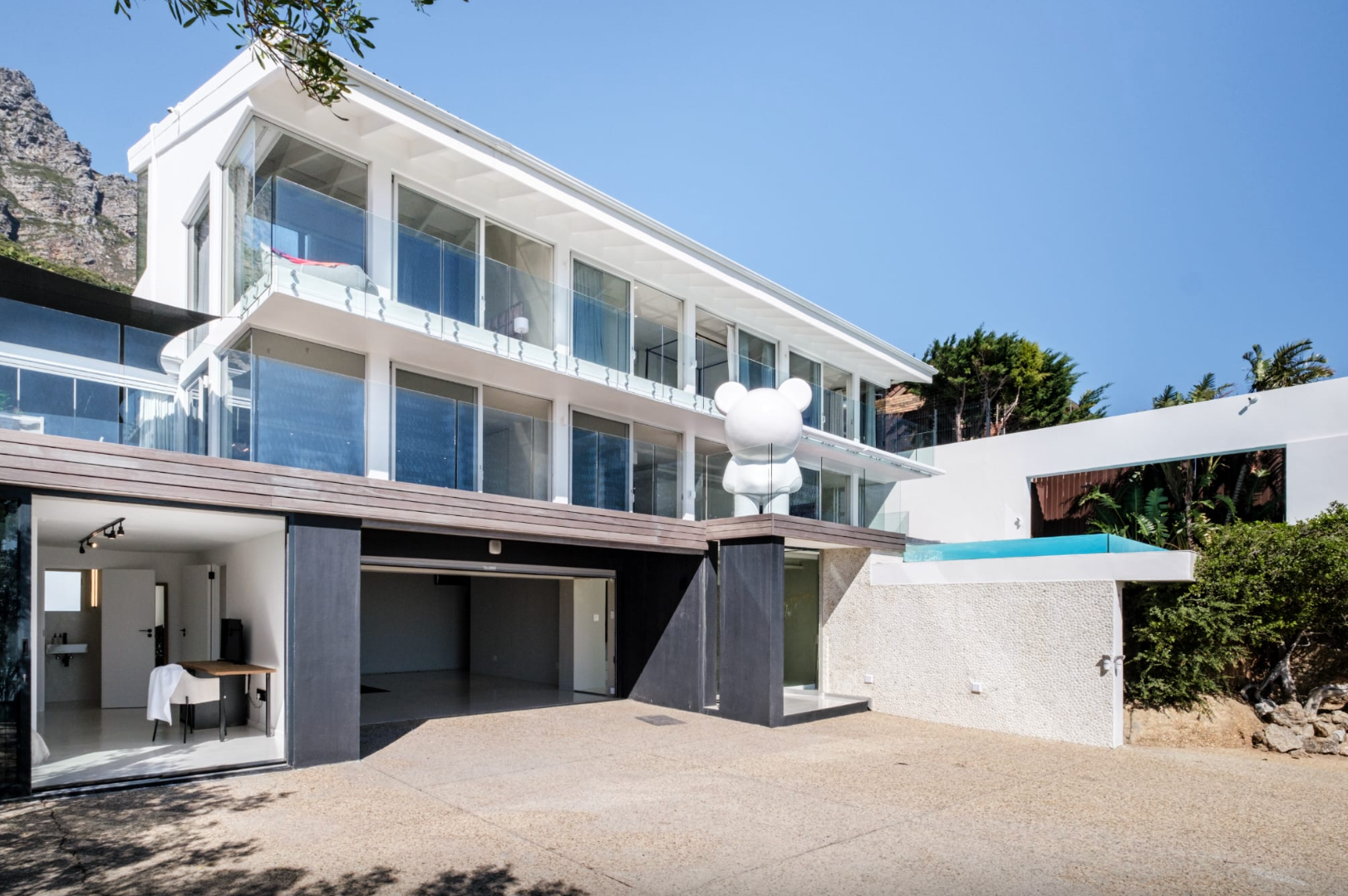 White modern house with glass windows, garage, and pool. A large white bear statue is on the balcony.