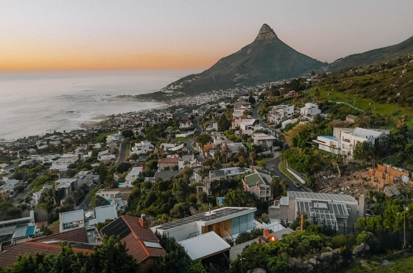 Coastal cityscape with Lion's Head mountain, sunset sky, houses, ocean view.