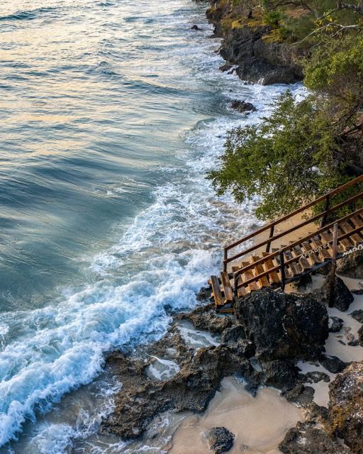 A wooden staircase leading up to the ocean with waves crashing on the rocks.