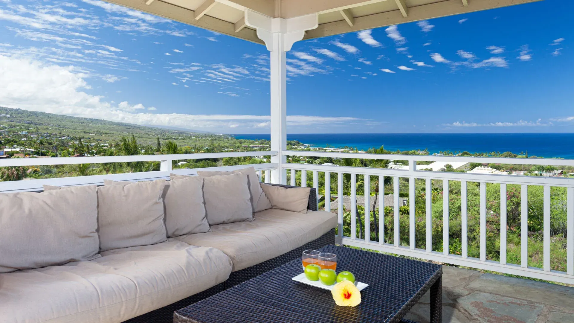 There is a couch and a table on the balcony with a view of the ocean.