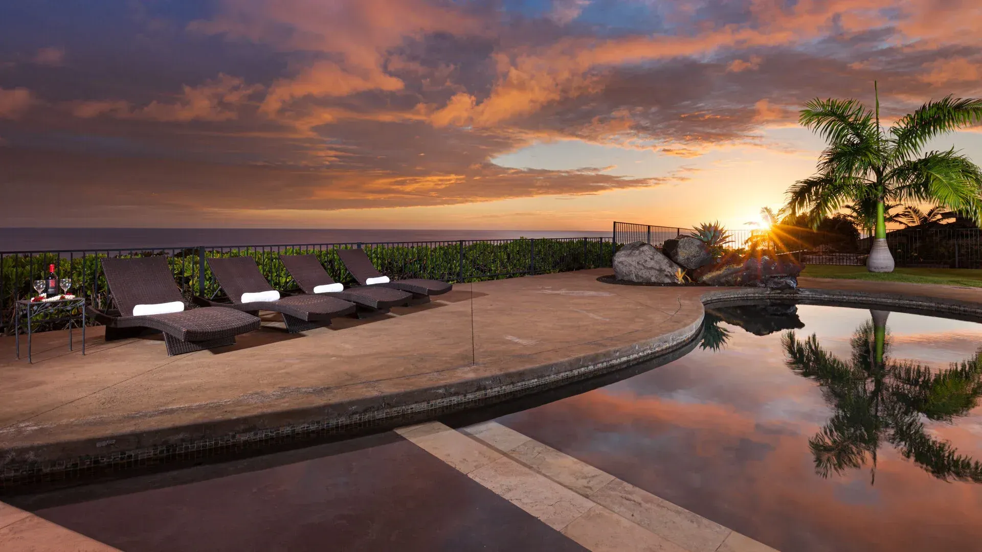A swimming pool with a view of the ocean at sunset.