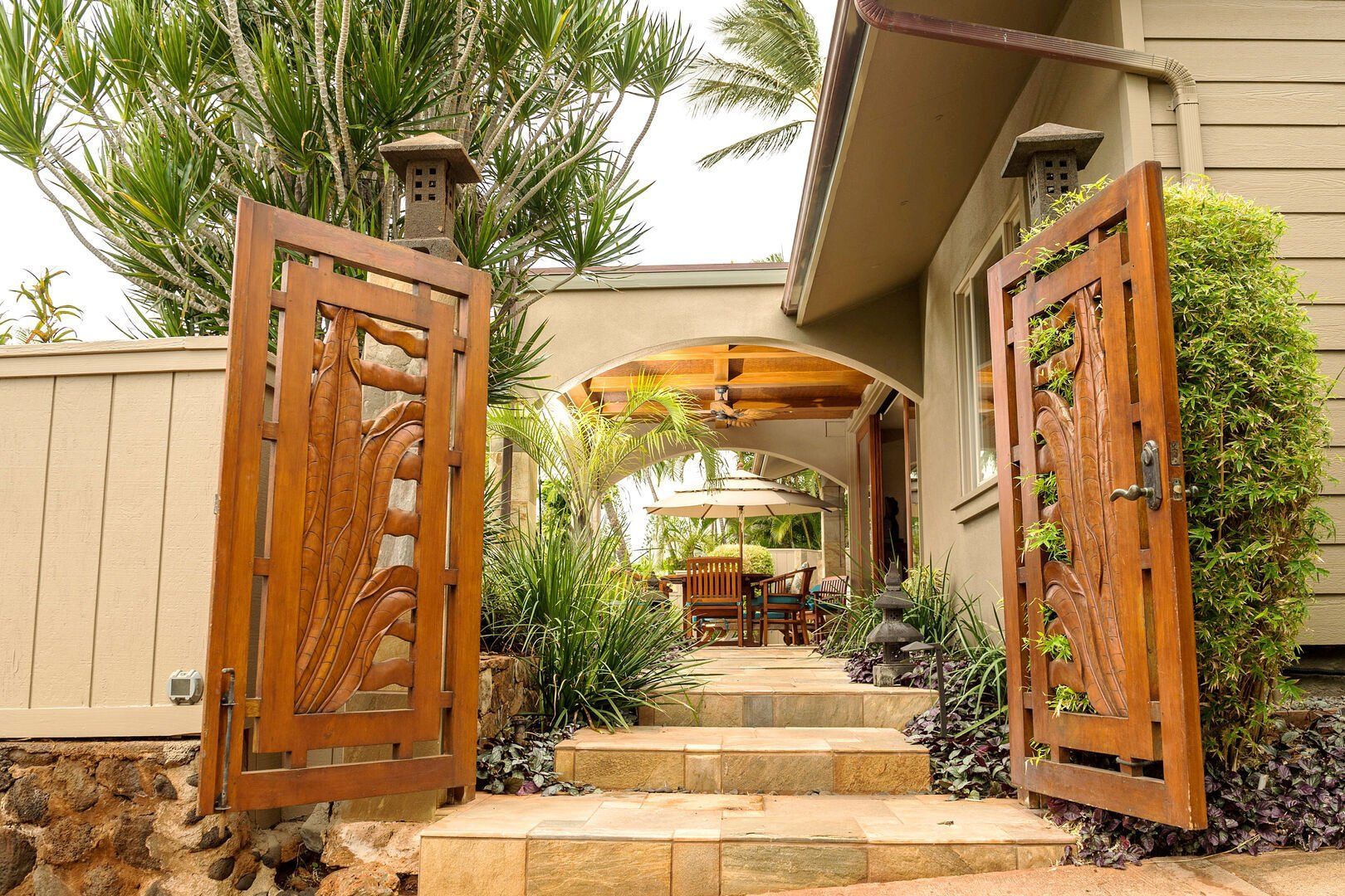 A wooden gate is open to a house with stairs leading up to it.