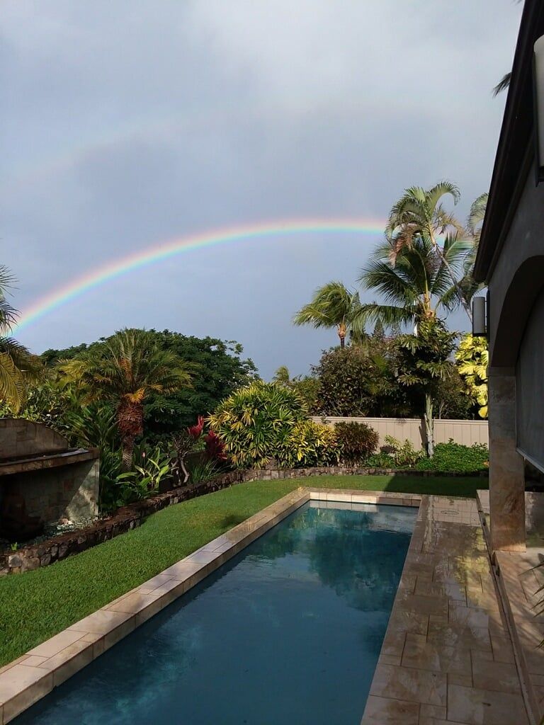 A rainbow is visible over a swimming pool in a backyard.