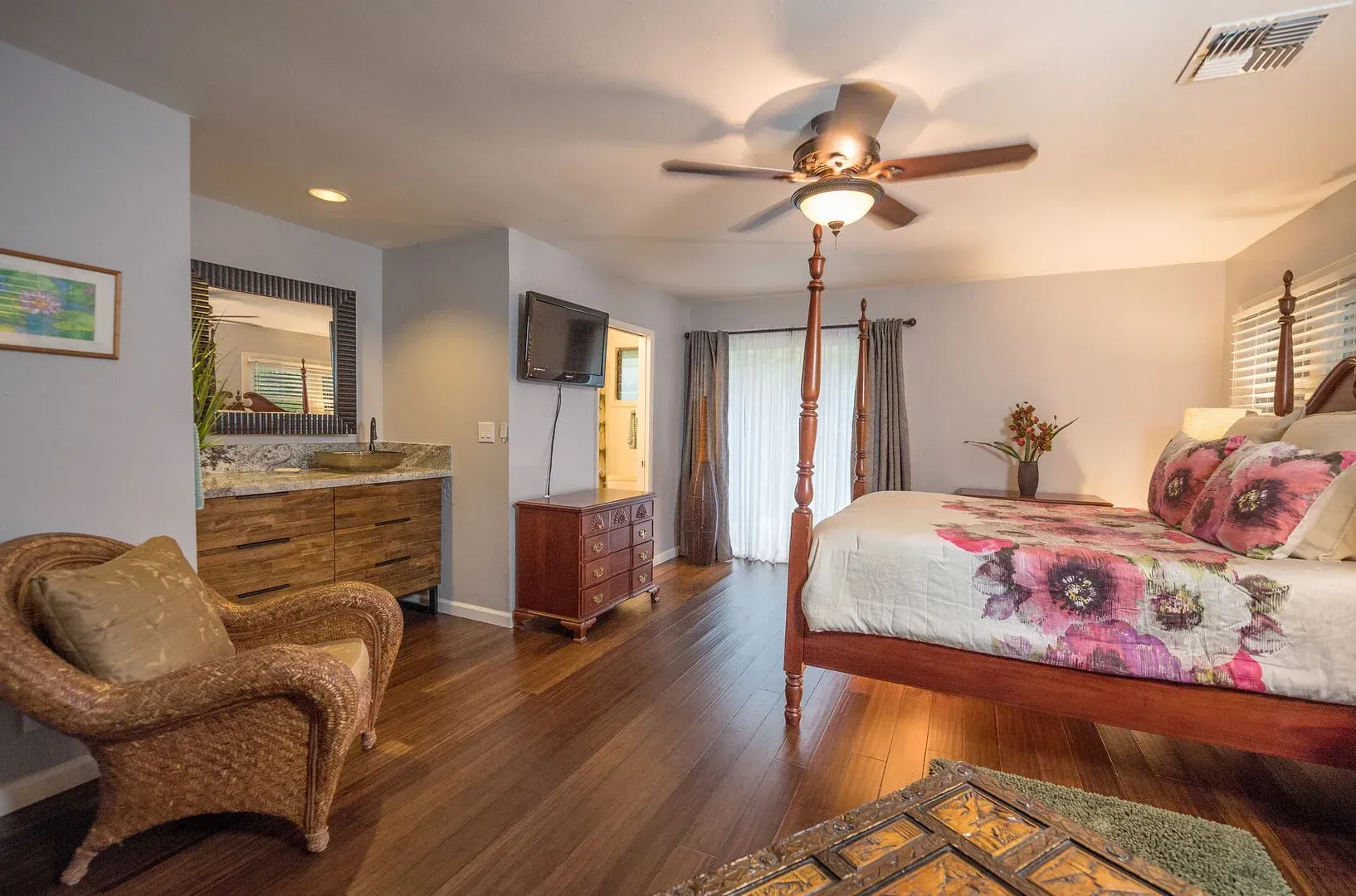 A bedroom with a four poster bed , chair , dresser and television.