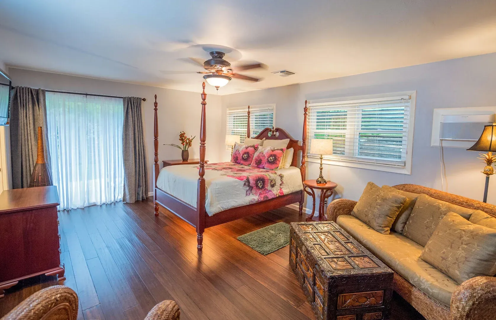 A bedroom with a four poster bed , a couch , and a ceiling fan.
