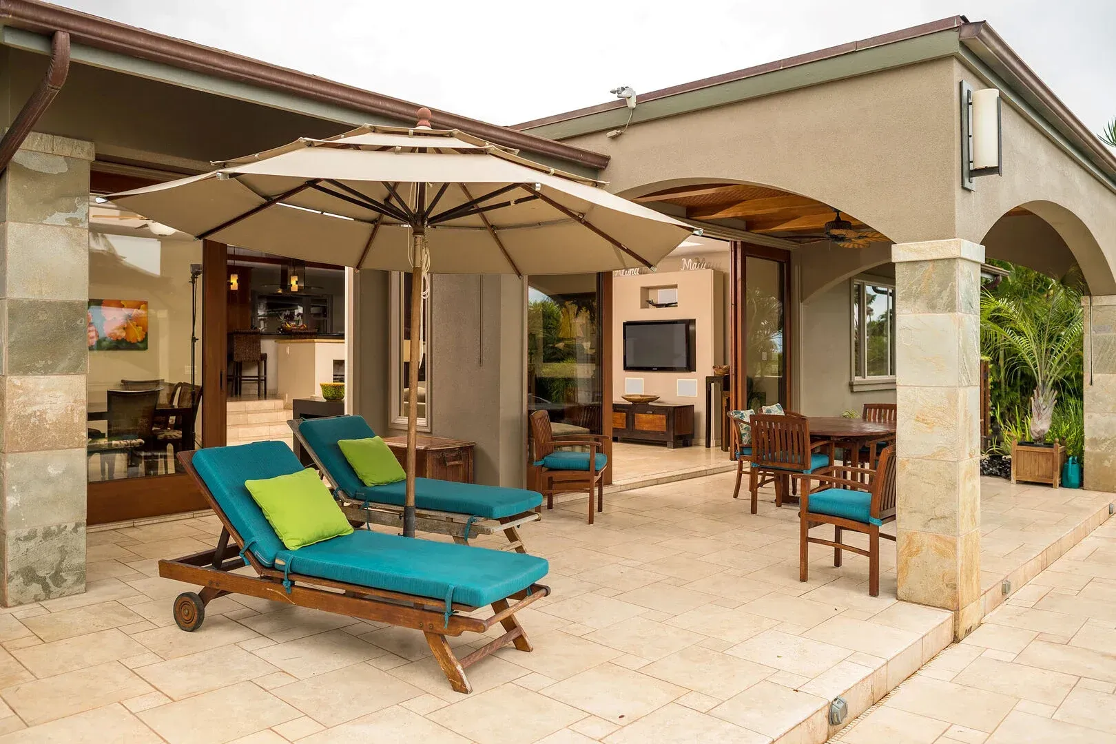 A patio with lounge chairs and an umbrella in front of a house.