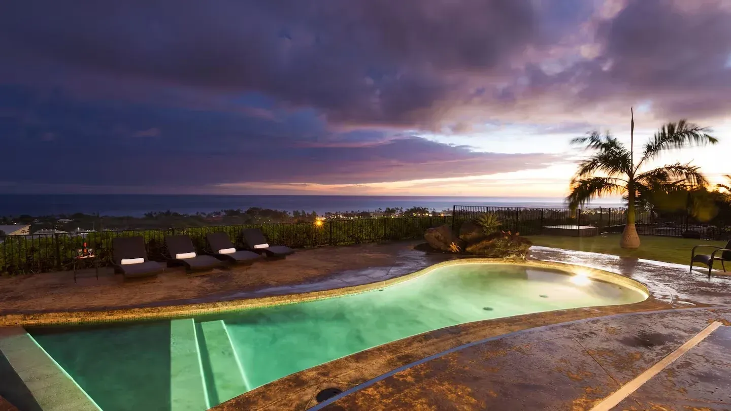 A large swimming pool with a view of the ocean at sunset.