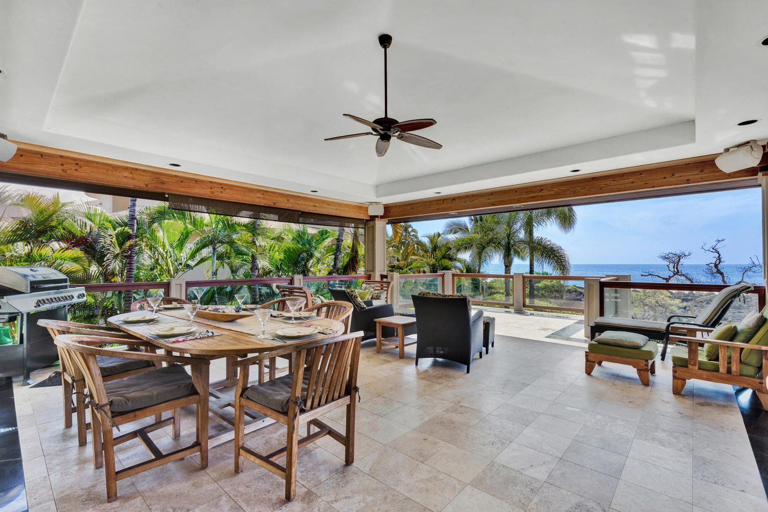 Outdoor dining area with ocean view; wooden table, chairs, and ceiling fan.