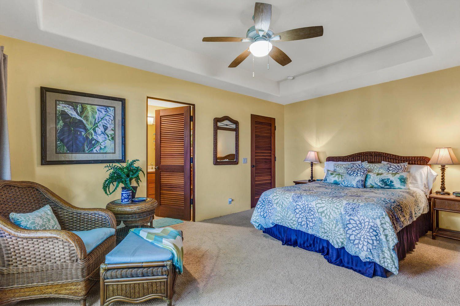 Bedroom with yellow walls, wicker furniture, floral bedspread, ceiling fan.