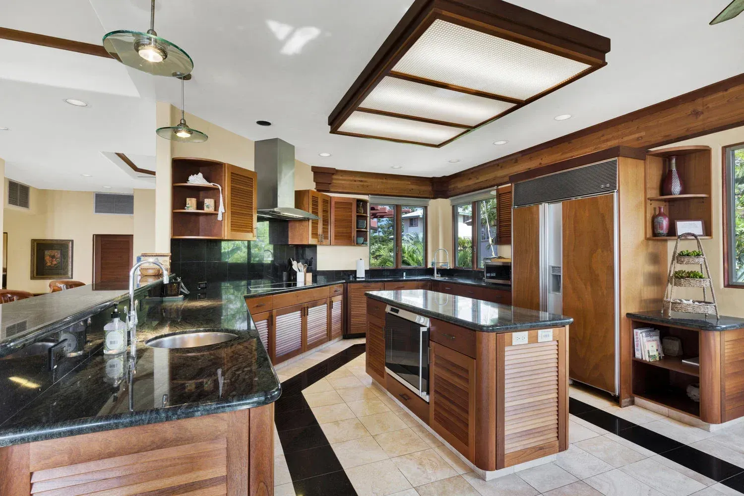 Luxury kitchen with dark granite counters, wooden cabinets, and island, on a tiled floor with black border.