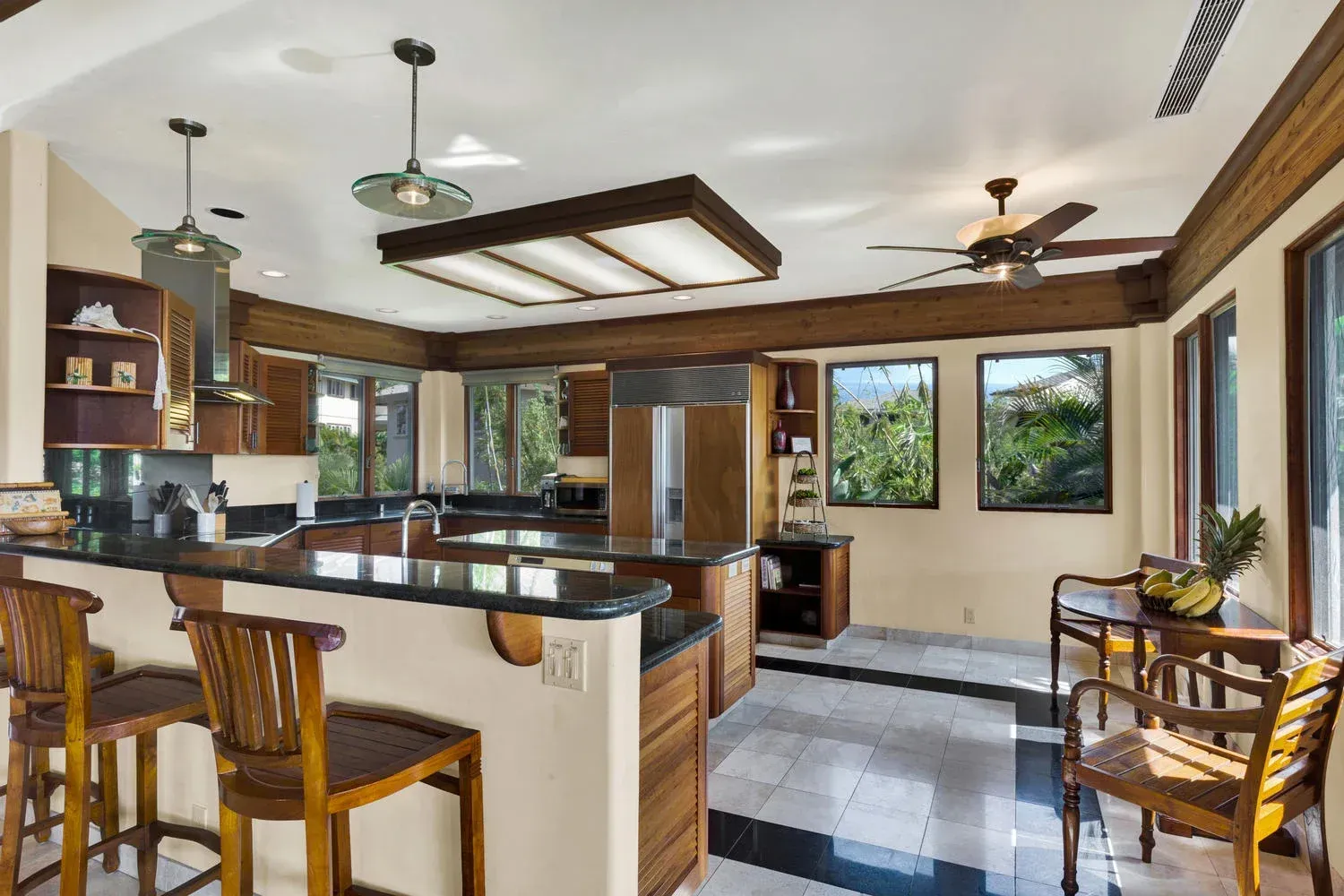 Kitchen with dark wood cabinets, bar stools, and a granite countertop; windows overlook greenery.