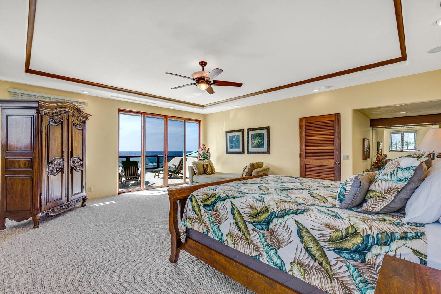 Spacious bedroom with ocean view, wooden bed and cabinet, yellow walls, and sliding glass doors.