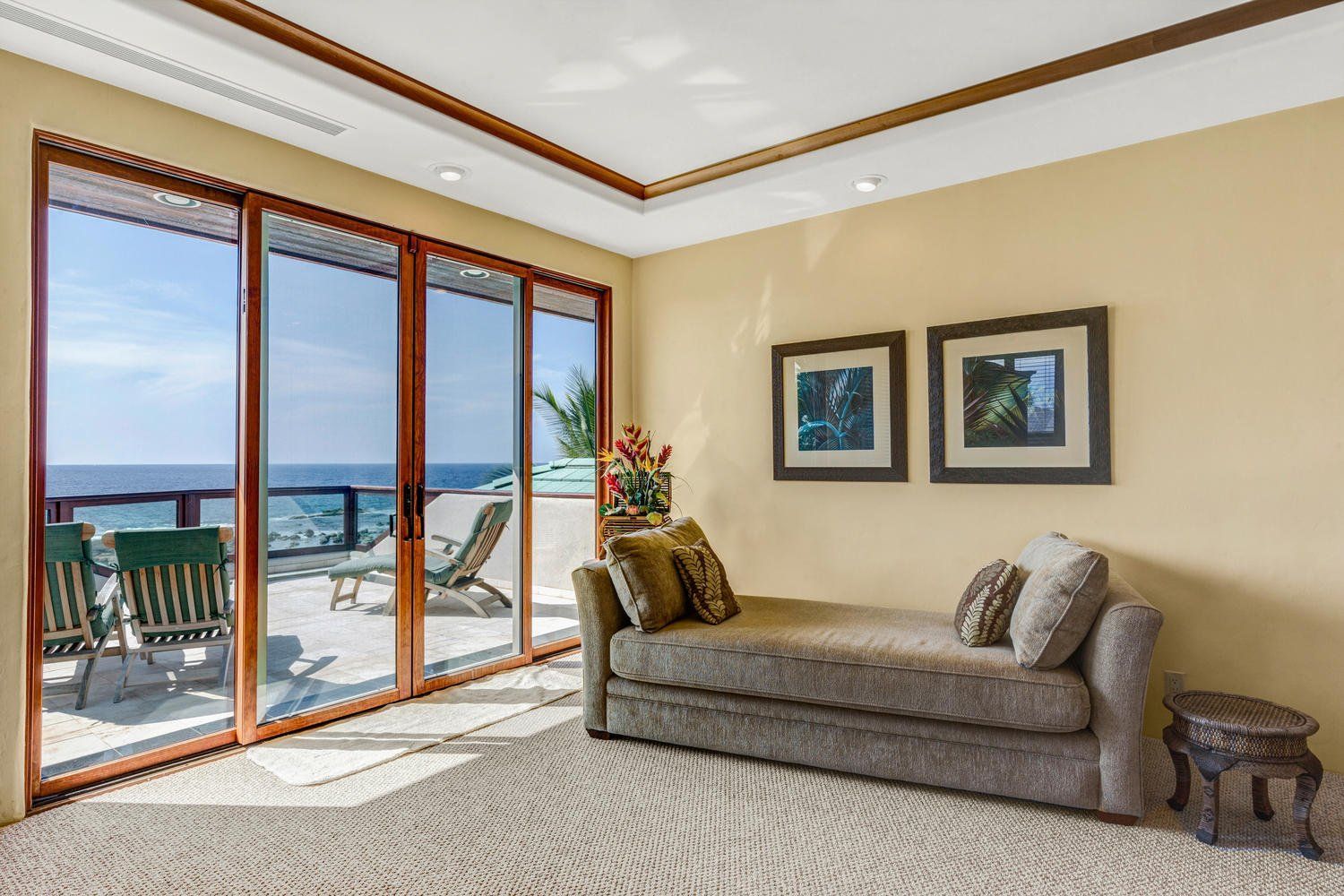 Interior room with ocean view through sliding glass doors, a chaise lounge, and two framed pictures.