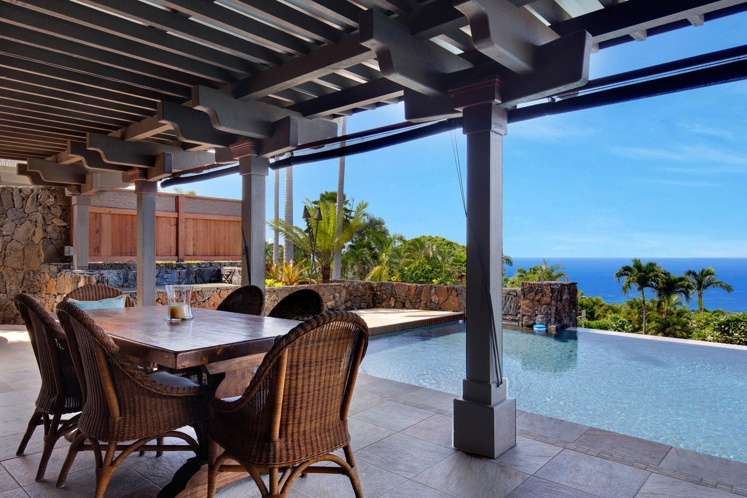 A patio with a table and chairs overlooking a pool and ocean