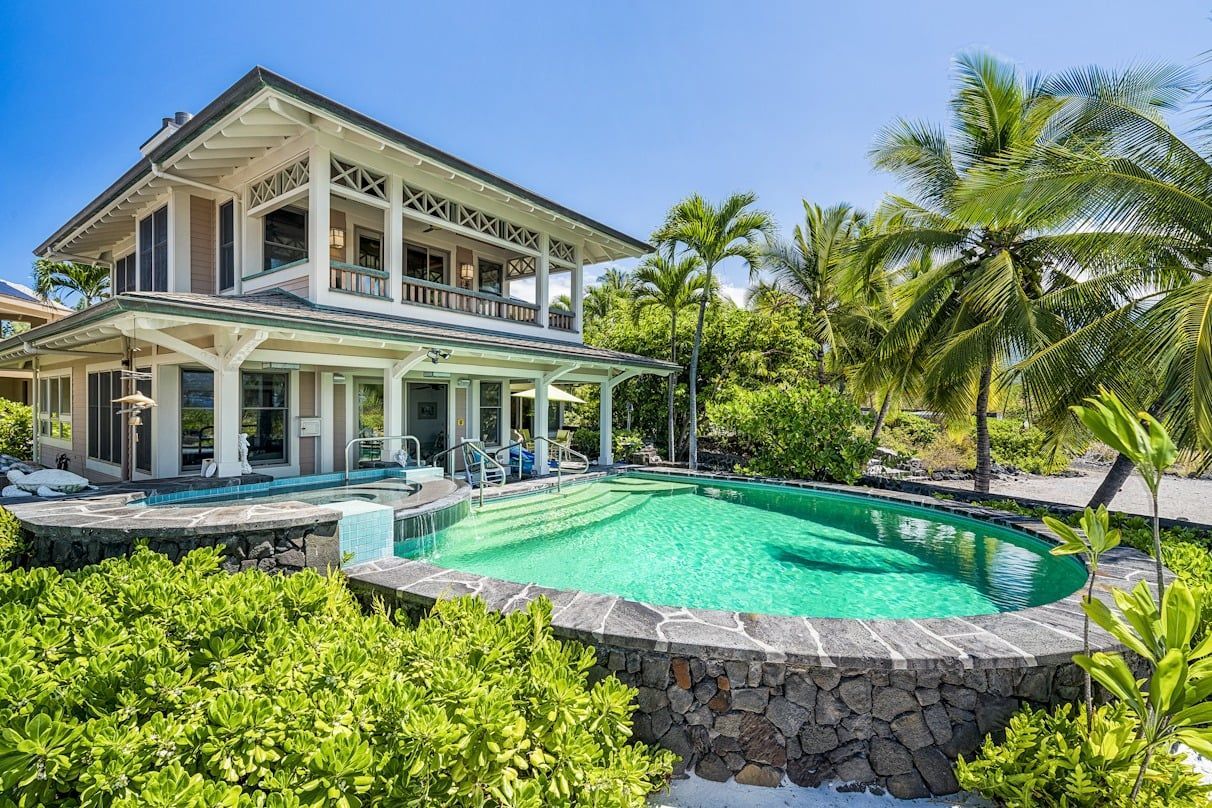 A large house with a swimming pool in front of it surrounded by palm trees.
