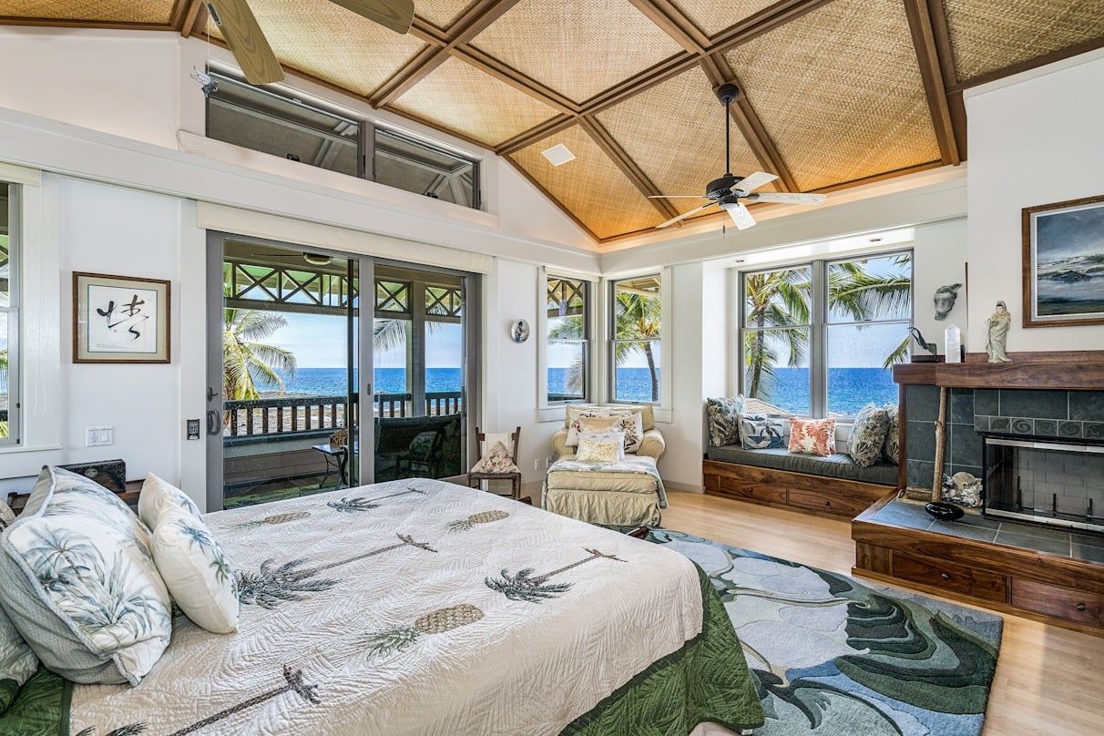 A bedroom with a bed , fireplace , chairs and a view of the ocean.